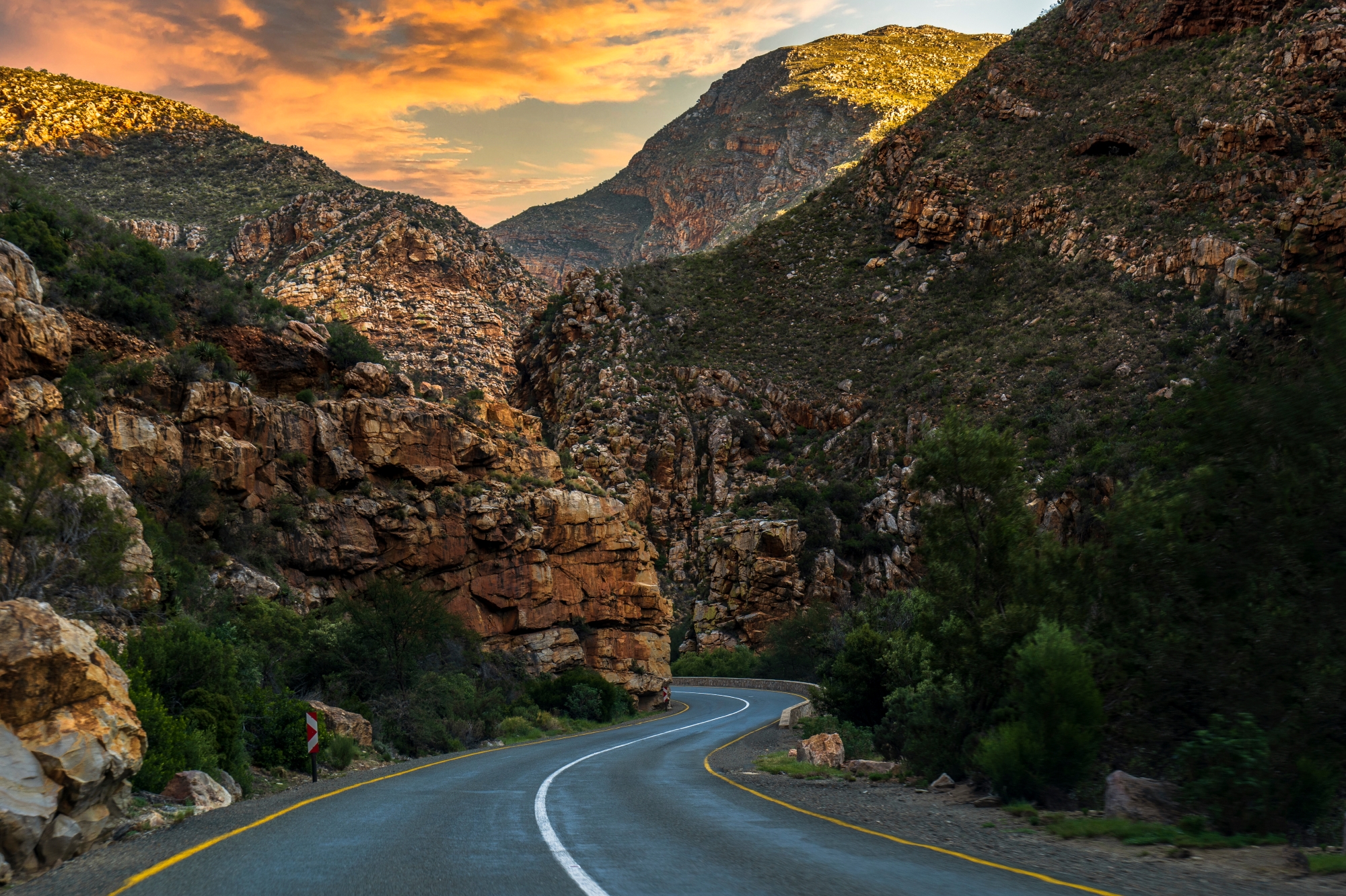 Scenic Route 62 Western Cape A smooth, winding road cuts through dramatic mountainous terrain, bordered by rugged cliffs and lush greenery.