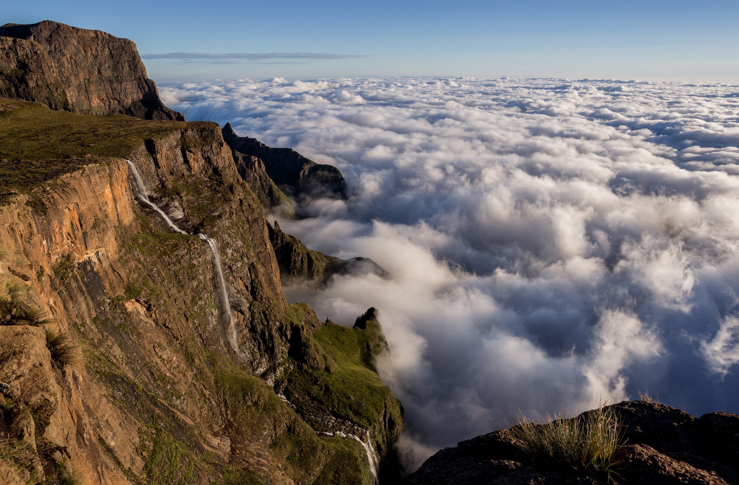 Tugela falls, Drakensburg, second highest waterfall in the world, taken from the top of the amphitheater Mist rolls through the dramatic cliffs of the Drakensberg, with lush green slopes leading down to a vast, open valley.