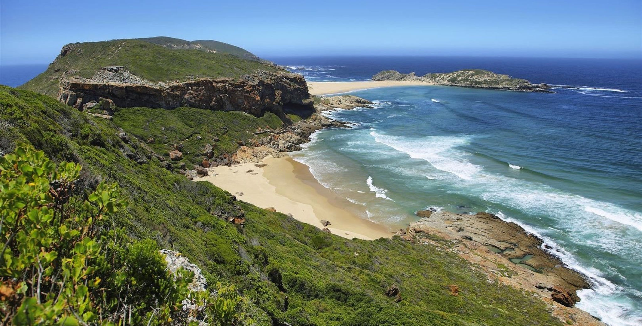 Idyllic beach in Robberg nature reserve in South Africa A breathtaking view of a secluded beach with golden sands and turquoise waters, nestled between lush green cliffs and the deep blue ocean.