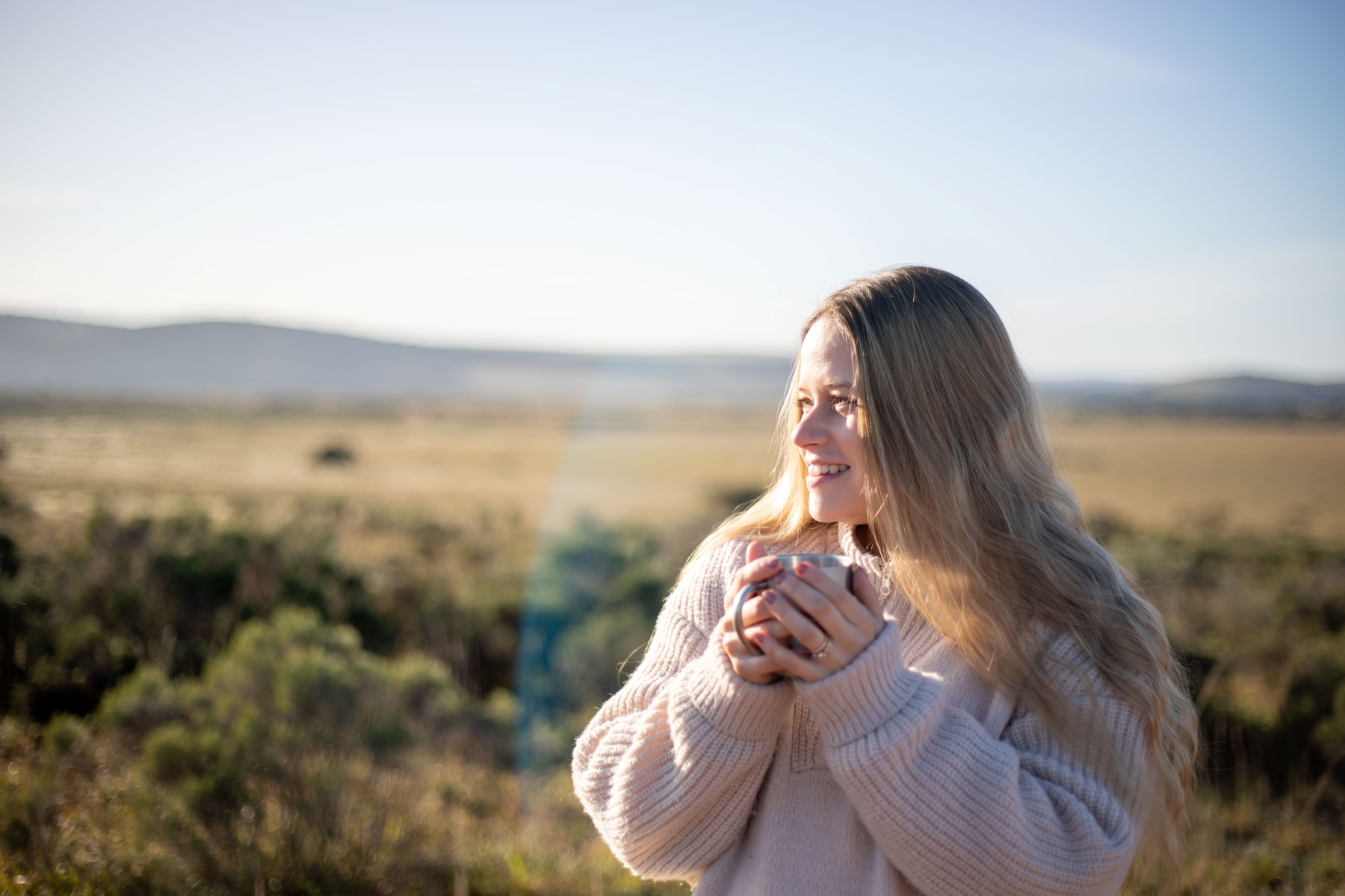luxury-safaris-with-rhino-africa-at-amakhala_D6A0970 Katharina in a cosy sweater holds a warm cup of tea, smiling as she gazes out over the vast African savanna during her babymoon safari.